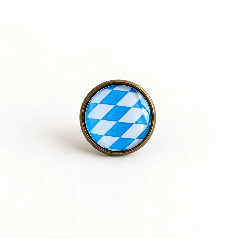 Minimalistisches Produktbild vom Bayern Pin – runder Pin mit blau-weißem Rautenmuster und altkupferfarbener Metallfassung Hauptbild