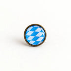 Minimalistisches Produktbild vom Bayern Pin – runder Pin mit blau-weißem Rautenmuster und altkupferfarbener Metallfassung