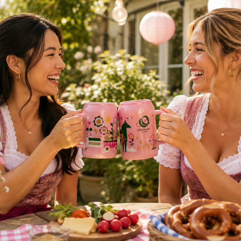 Zwei Freundinnen stoßen im Garten mit rosa Oktoberfest-Bierkrügen an