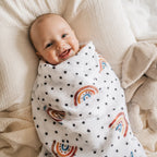 Lächelndes Baby eingewickelt in ein Mulltuch im Regenbogen-Design