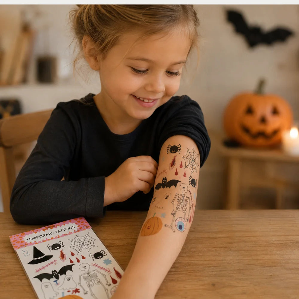 Kind zeigt temporäre Halloween-Tattoos mit Spinne, Fledermaus, Skelett und Kürbis auf dem Unterarm.