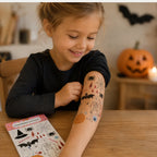 Kind zeigt temporäre Halloween-Tattoos mit Spinne, Fledermaus, Skelett und Kürbis auf dem Unterarm.