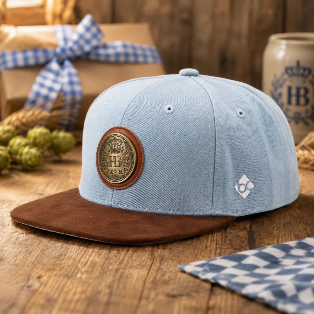 Hellblaue Hofbräuhaus München Snapback-Cap auf rustikalem Holztisch mit bayerischer Dekoration