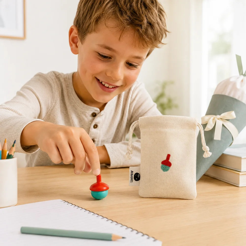 Schulkind spielt mit Holzkreisel in Mint und Rot, daneben Baumwollbeutel und Schultüte