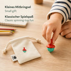 Kind spielt mit handbemaltem Holzkreisel, daneben der Baumwollbeutel – kleines Mitbringsel für Kinder