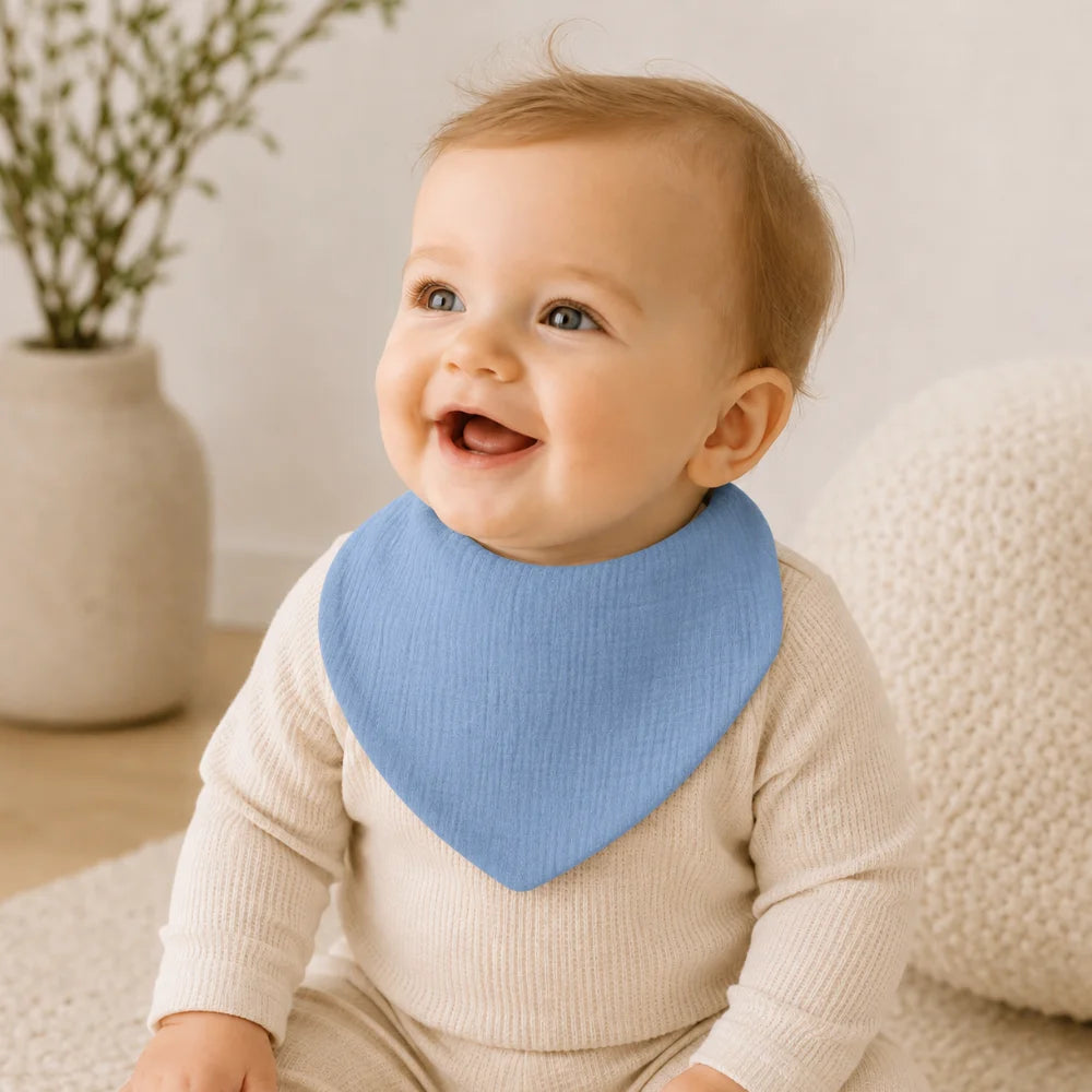 Baby trägt ein blaues Musselin-Lätzchen in der Farbe Dusty Blue
