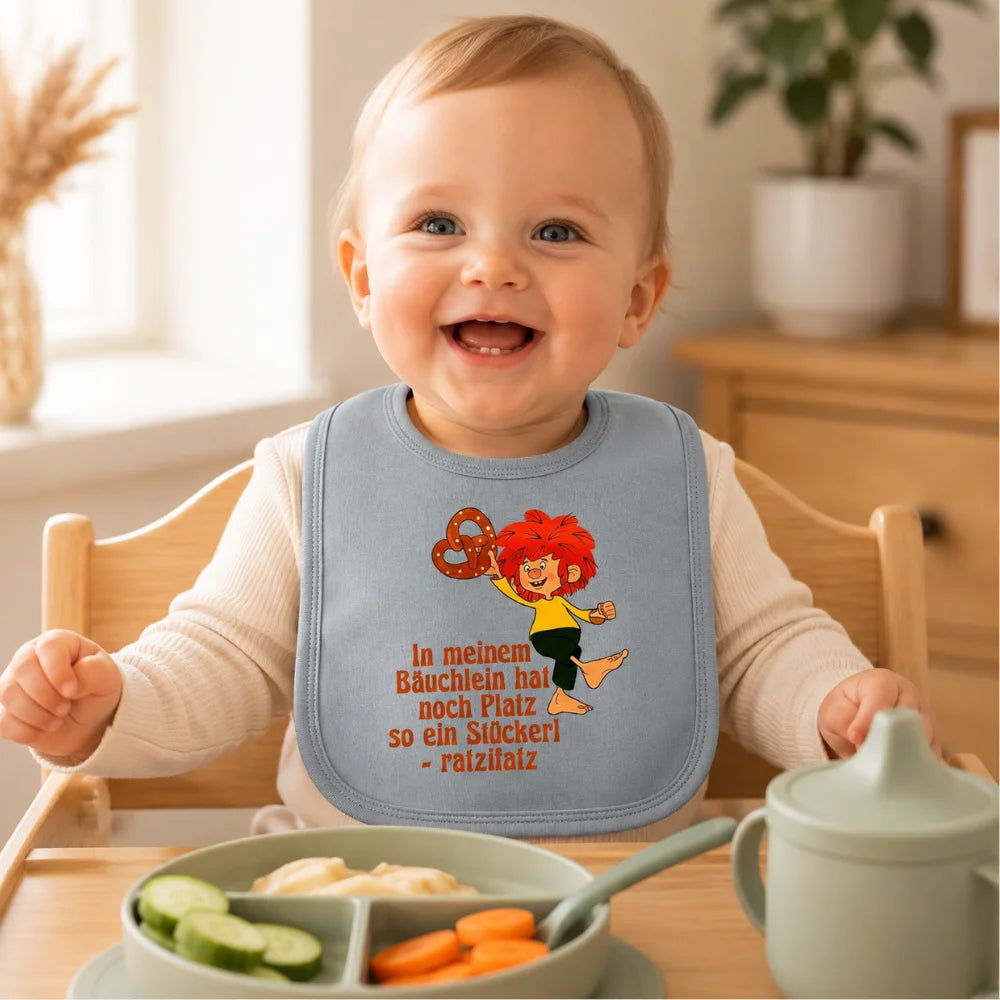 Baby trägt graues Pumuckl Lätzchen mit Brezelmotiv beim Essen im Hochstuhl
