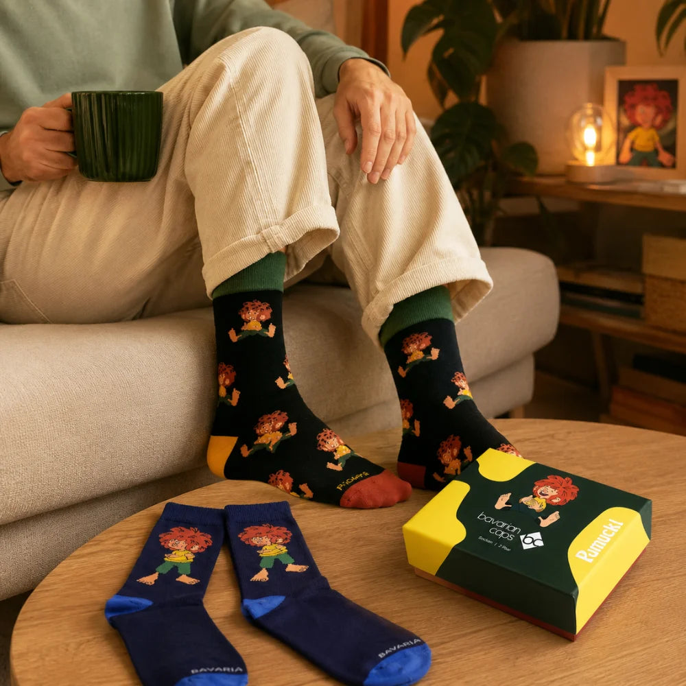 Person trägt Pumuckl Socken im Alltag, zweites Paar und Geschenkbox liegen daneben