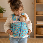 Kind trägt eine Puppe im blauen Puppentragesack mit Blumenmuster