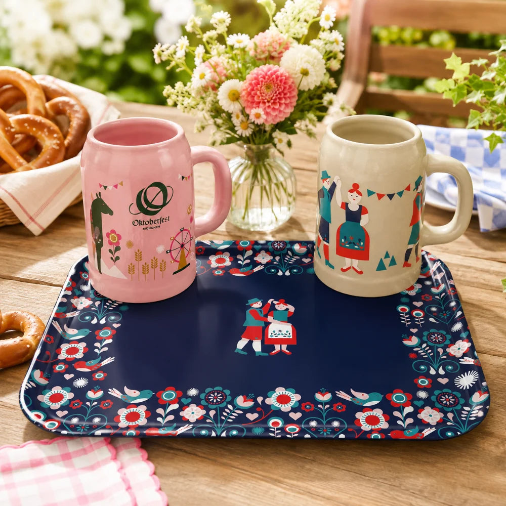 Oktoberfest-Tablett mit rosa und grauem Bierkrug, Brezen und Blumen im Garten