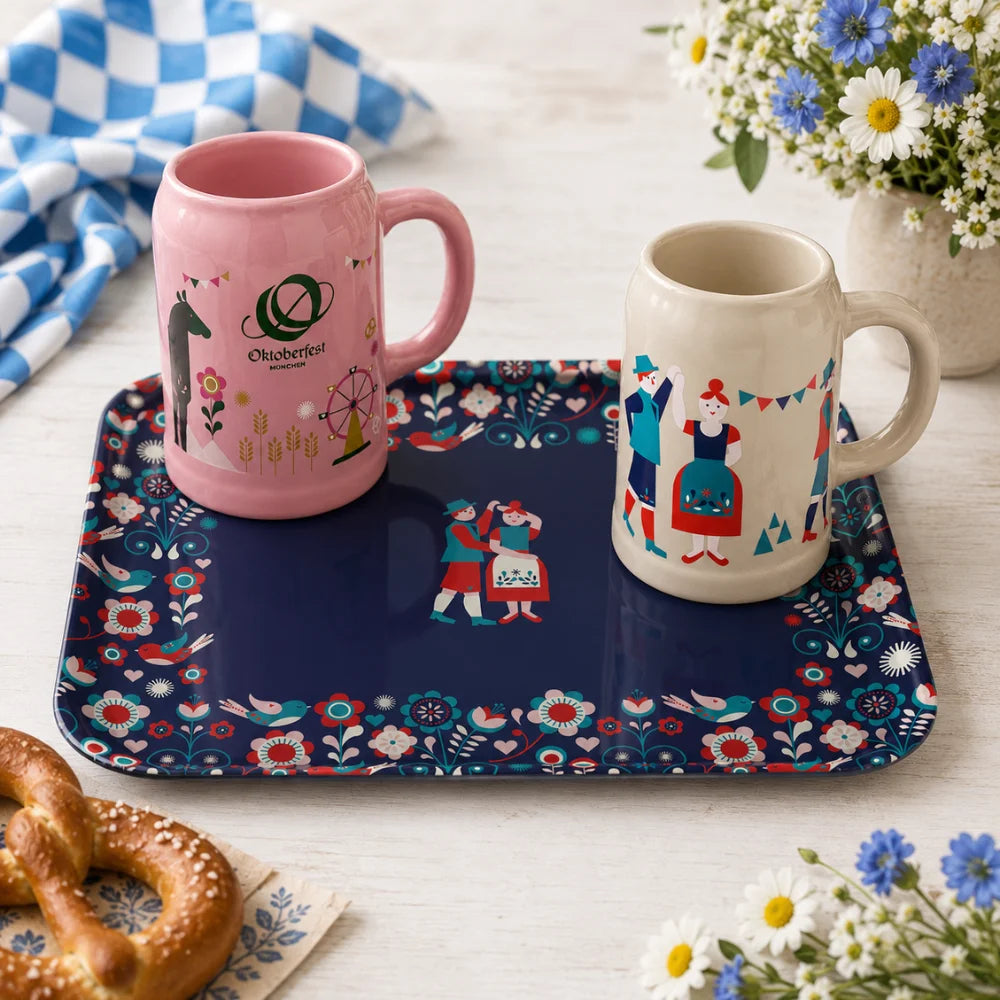 Oktoberfest-Tablett mit rosa und grauem Bierkrug, Brezen und Blumen auf gedecktem Tisch