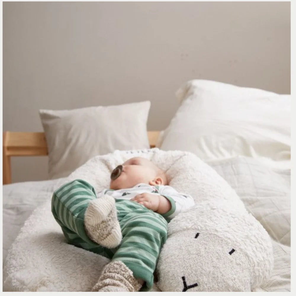 Baby liegt entspannt im EFIE Stillkissen Schaf auf einem Bett in heller, gemütlicher Umgebung.