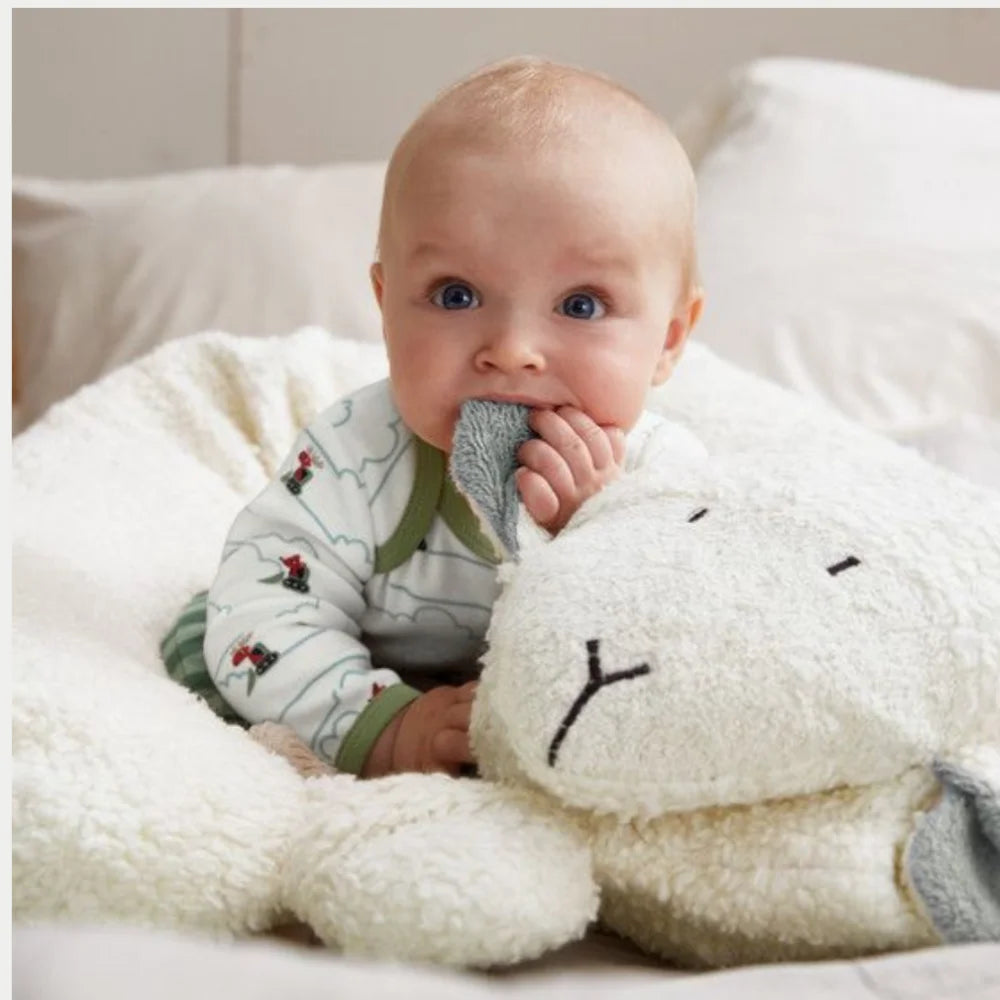 Baby sitzt gestützt im EFIE Stillkissen Schaf und hält das weiche graue Ohr des Schafkopfs.