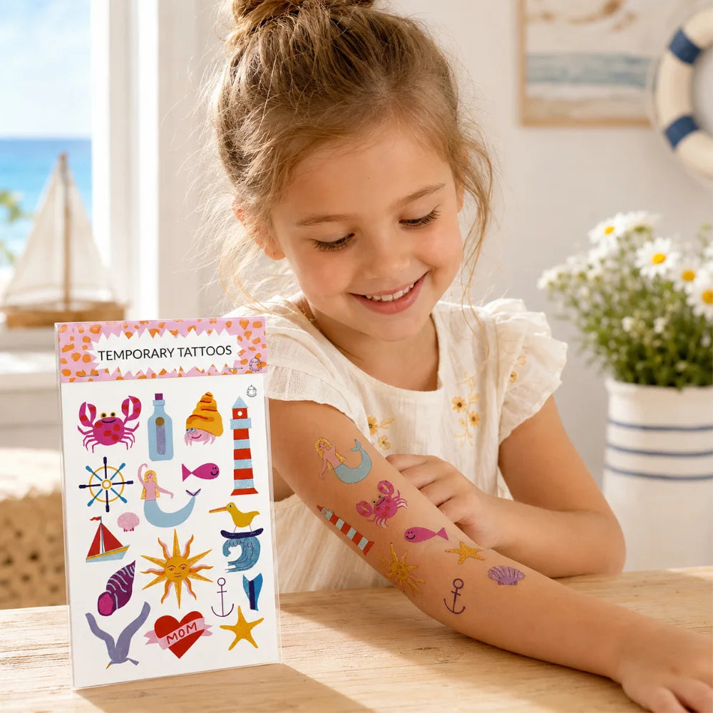 Kind zeigt maritime temporäre Tattoos mit Meerjungfrau, Krebs, Leuchtturm, Fisch und Anker auf dem Unterarm.