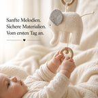 Baby liegt im Bett und greift nach Elefanten-Spieluhr mit Holzring, sanfte Stoffoberfläche und ruhige Einschlafszene