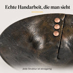 Detailaufnahme einer handgeschmiedeten Eisenschale mit strukturierter Oberfläche, Bruchkante und drei Kupfernieten