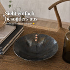 Handgeschmiedete Eisenschale mit Kupfernieten auf Holztisch neben Büchern und Glasvase in stilvollem Wohnambiente